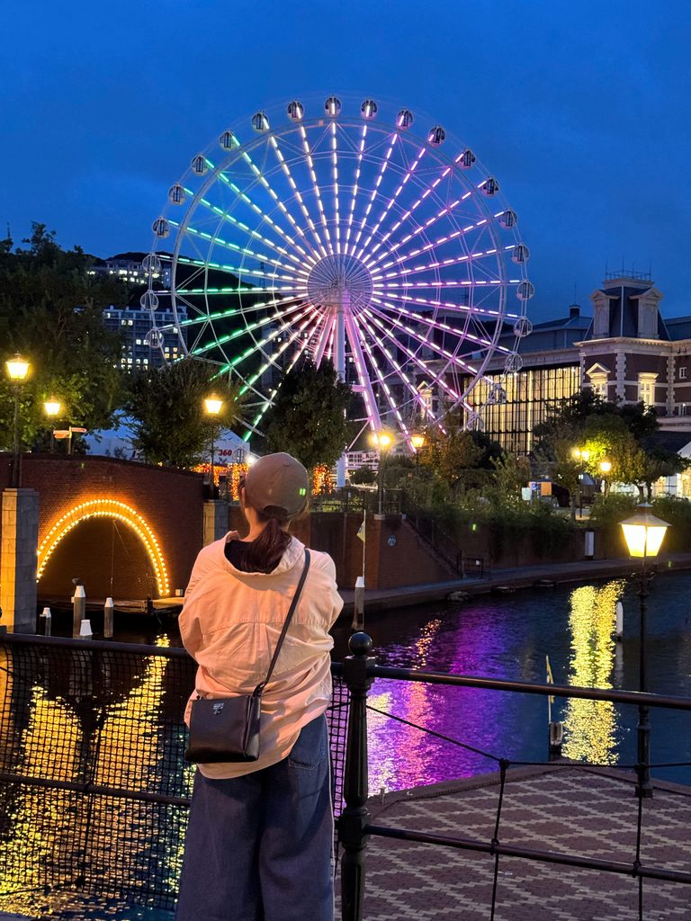 Looking out at the rainbow-lit Ferris wheel reflected in the canal at Huis Ten Bosch