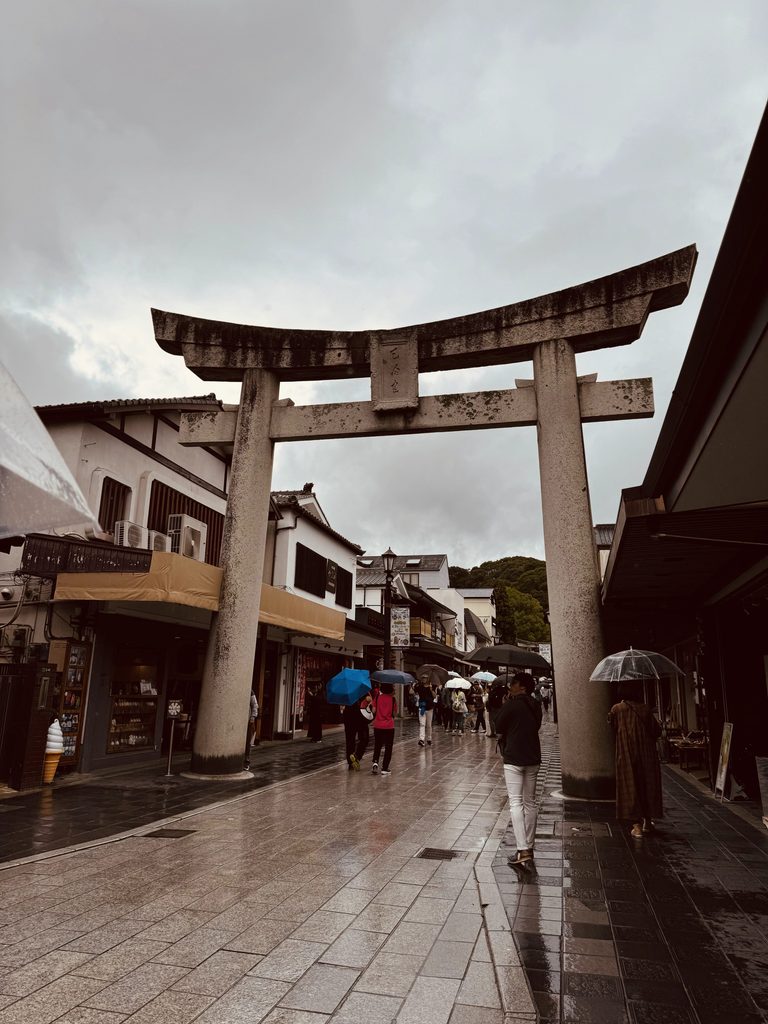The stone torii gate on the rainy approach to Dazaifu Tenmangu, lined with shops