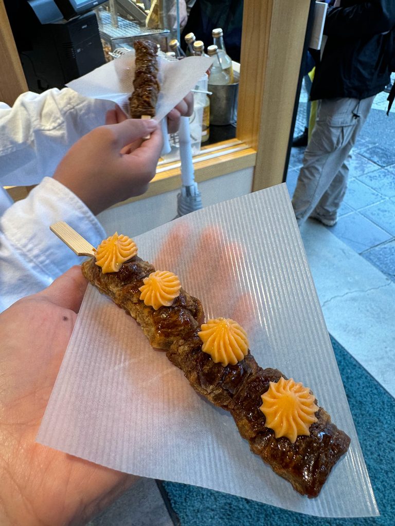 A freshly grilled skewer topped with piped sauce, eaten on the Dazaifu approach