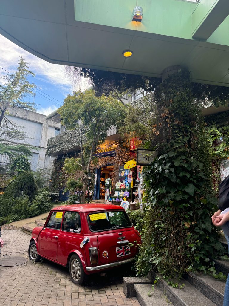 A red Mini parked in front of an ivy-covered shop along Yunotsubo Street in Yufuin