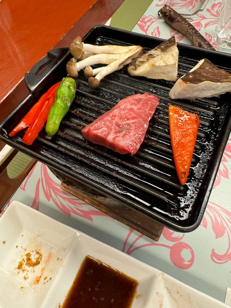 Wagyu beef, salmon, mushrooms and peppers cooking on a tabletop grill at dinner